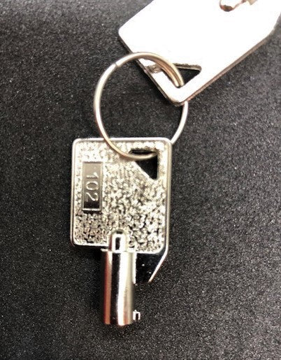 Close-up of an AED Shop Key 102, a silver key with a tag labeled "192," resting on a black surface. The non-interchangeable key is securely attached to a keyring.