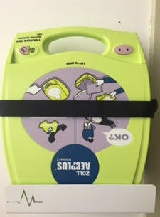 A yellow Zoll AED Plus with illustrated instructions is secured to the wall on an AED Shop Universal AED Bracket.