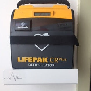 A LIFEPAK CR Plus defibrillator, secured on a rugged AED Shop Universal AED Bracket with adjustable depth, is attached to a wall mount, ready for emergency use.