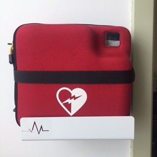 A red defibrillator case featuring a white heart and lightning bolt symbol, securely mounted on the AED Shop's rugged Universal AED Bracket.