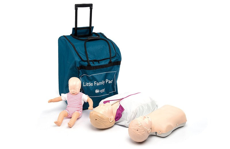 Two adult CPR manikins laying on the ground besides an infant CPR manikin leaning against a cyan bag with black handles.